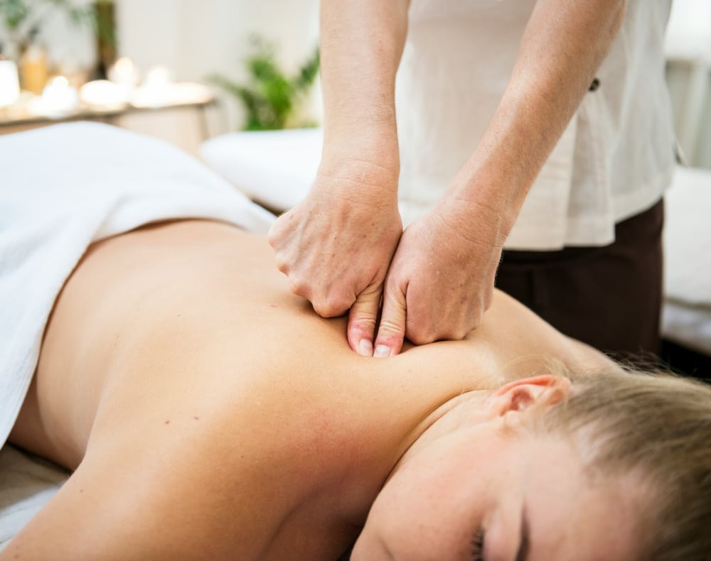 Une personne pratique la spino-réflexologie (ou réflexologie dorsale) sur une femme allongée sur le ventre, dos nu, sur une table de massage